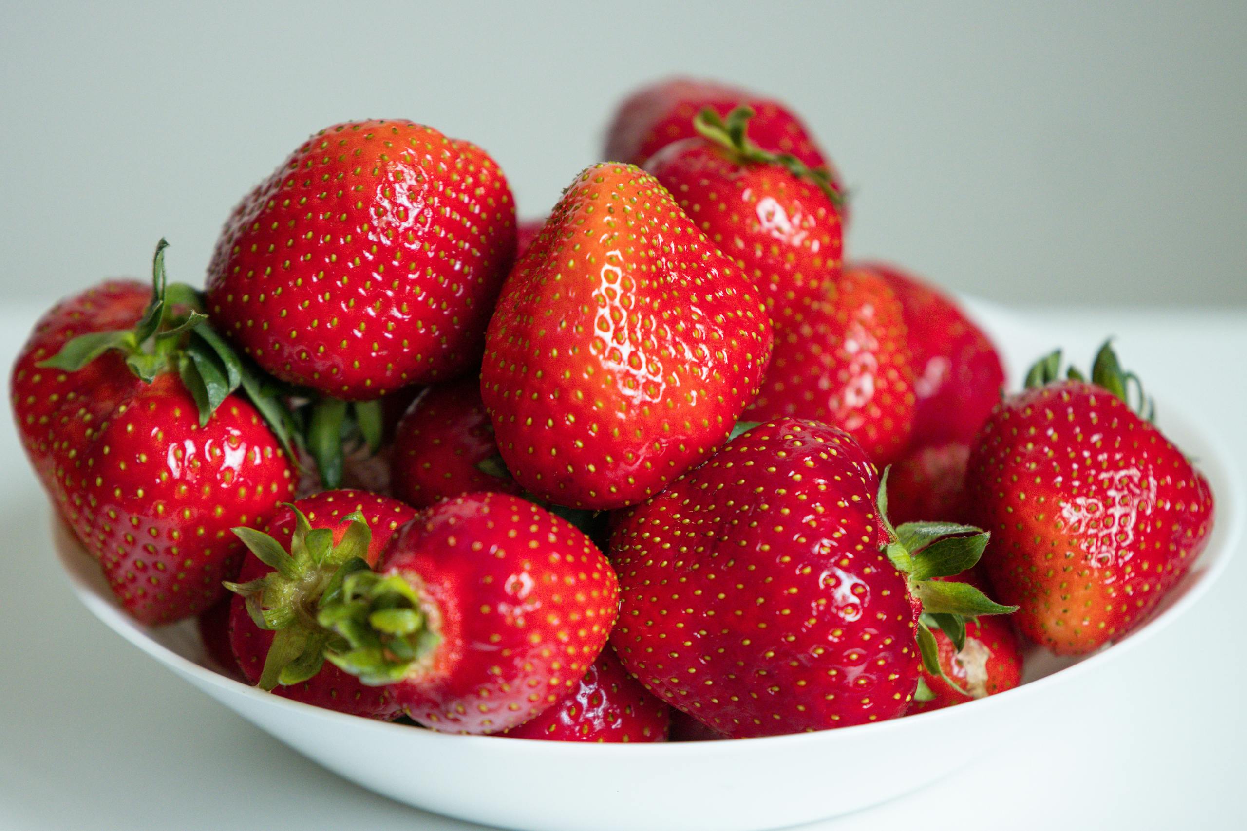 A vibrant close-up of fresh red strawberries in a white bowl, perfect for healthy eating representation.